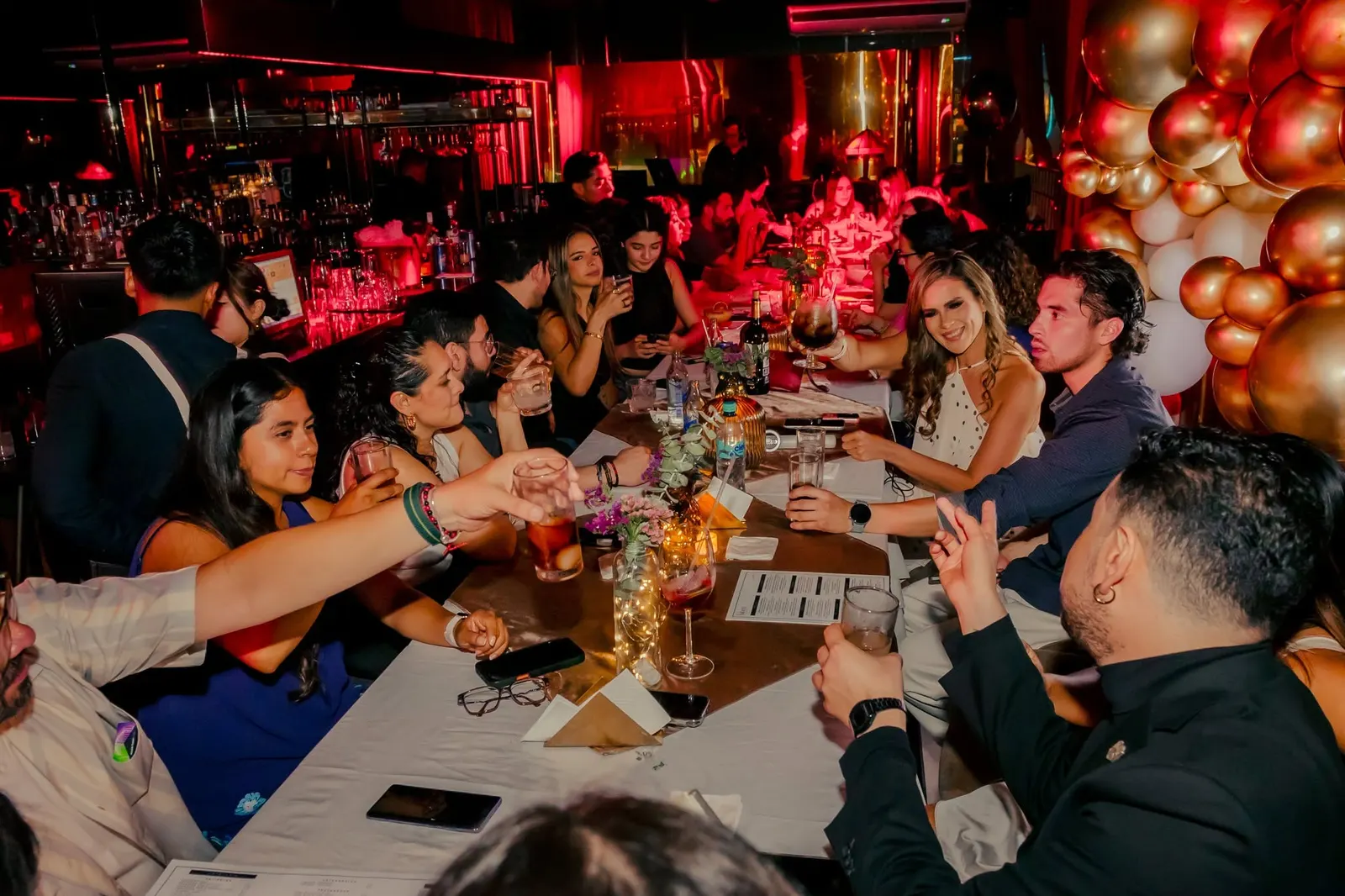 Un grupo brindando en una mesa larga de Nuberu decorada con globos dorados